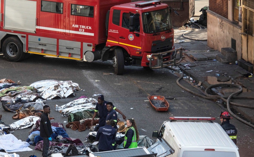epa10830422 Fire crews and emergency staff stand next to the covered bodies of the victims as they gather at the site of a fire that broke out at the five-storey building in the city centre, in Johannesburg, South Africa, 31 August 2023. More than 60 peop
