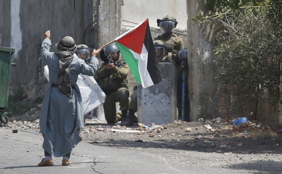 Ηλικωμένος Παλαιστίνιος ανεμίζει σημαία της Παλαιστίνης μπροστά σε πάνοπλους Ισραηλινούς στρατιώτες στη Δυτική Όχθη / EPA-ALAA BADARNEH